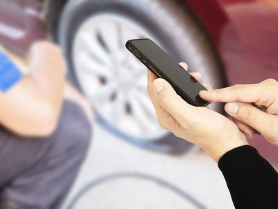 Man is using mobile phone calling somebody over car flat tire background